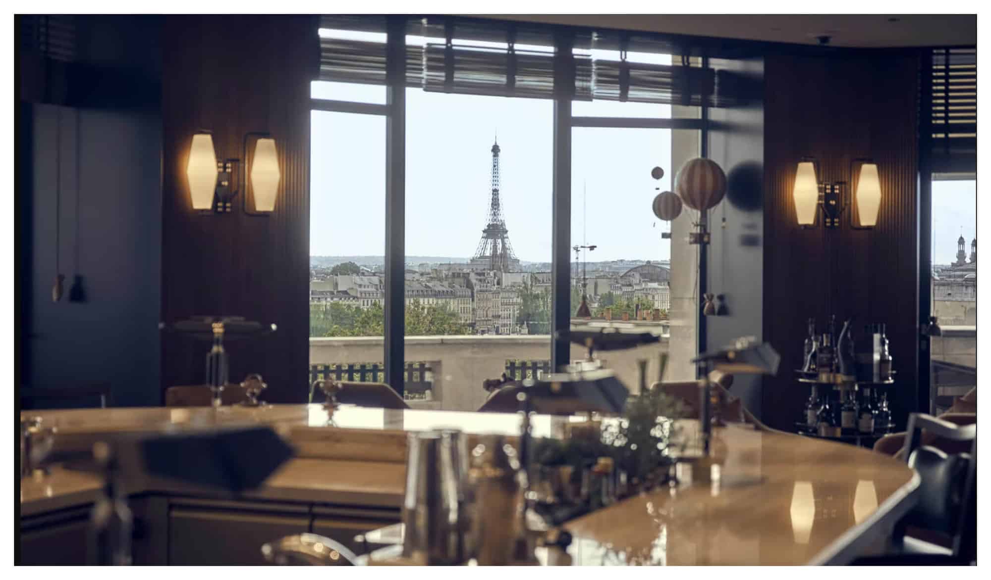 A bar with dark decor and marbled tables, overlooking the Eiffel Tower