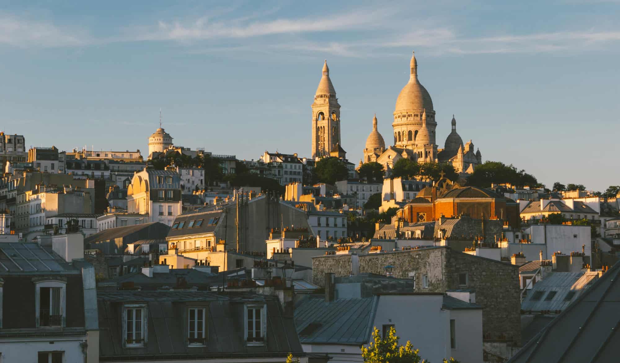 A shot at golden hour of Montmartre rooftops with a view of Sacre Coeur lit by the setting sun.