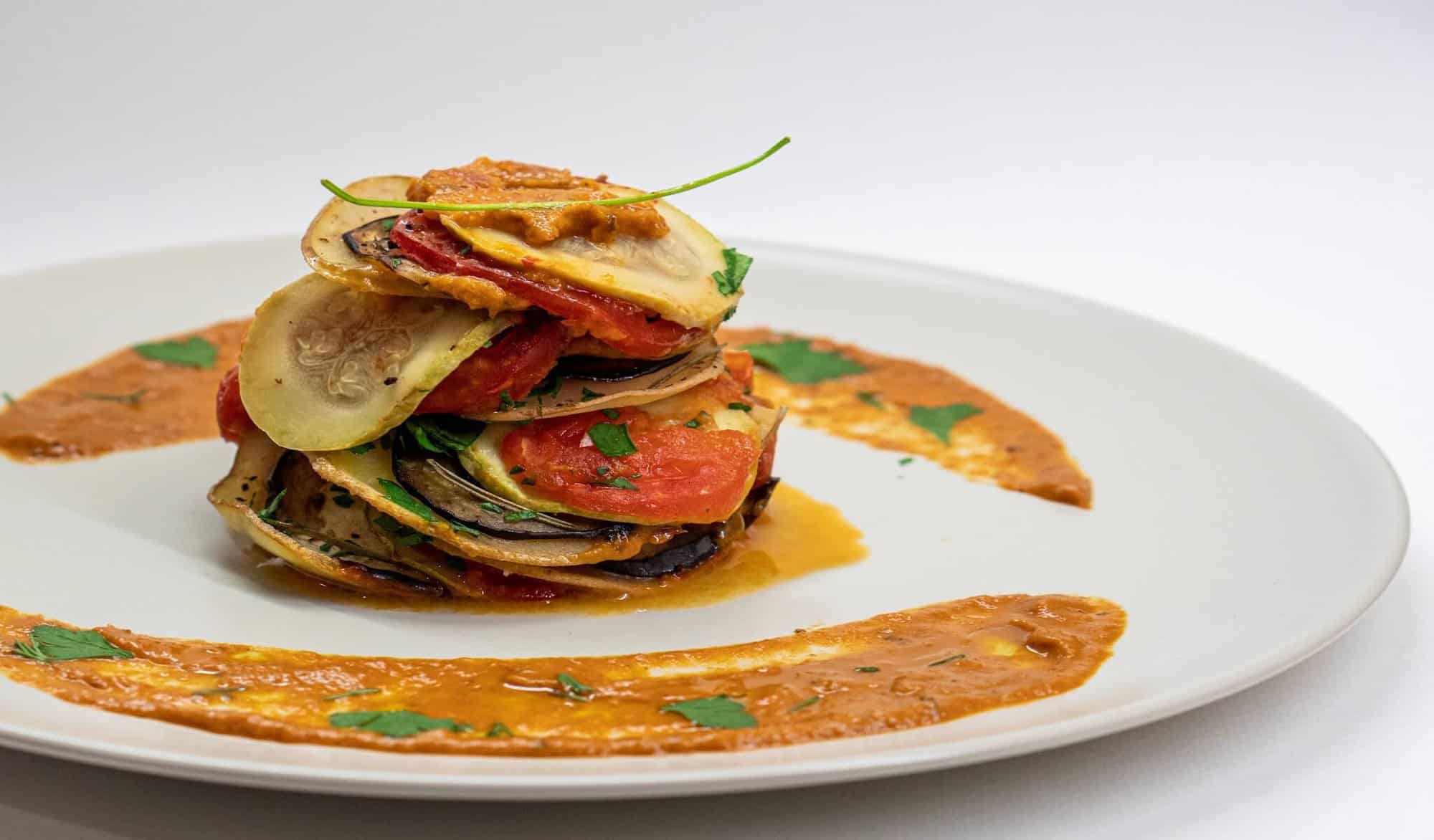 A classic French dish of Ratatouile with colorful sliced vegetables and a garnish of tomato sauce.