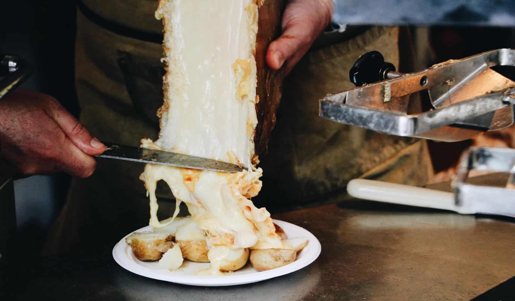 A man scrapes a half-moon slice of raclette cheese to a plate of potatoes.