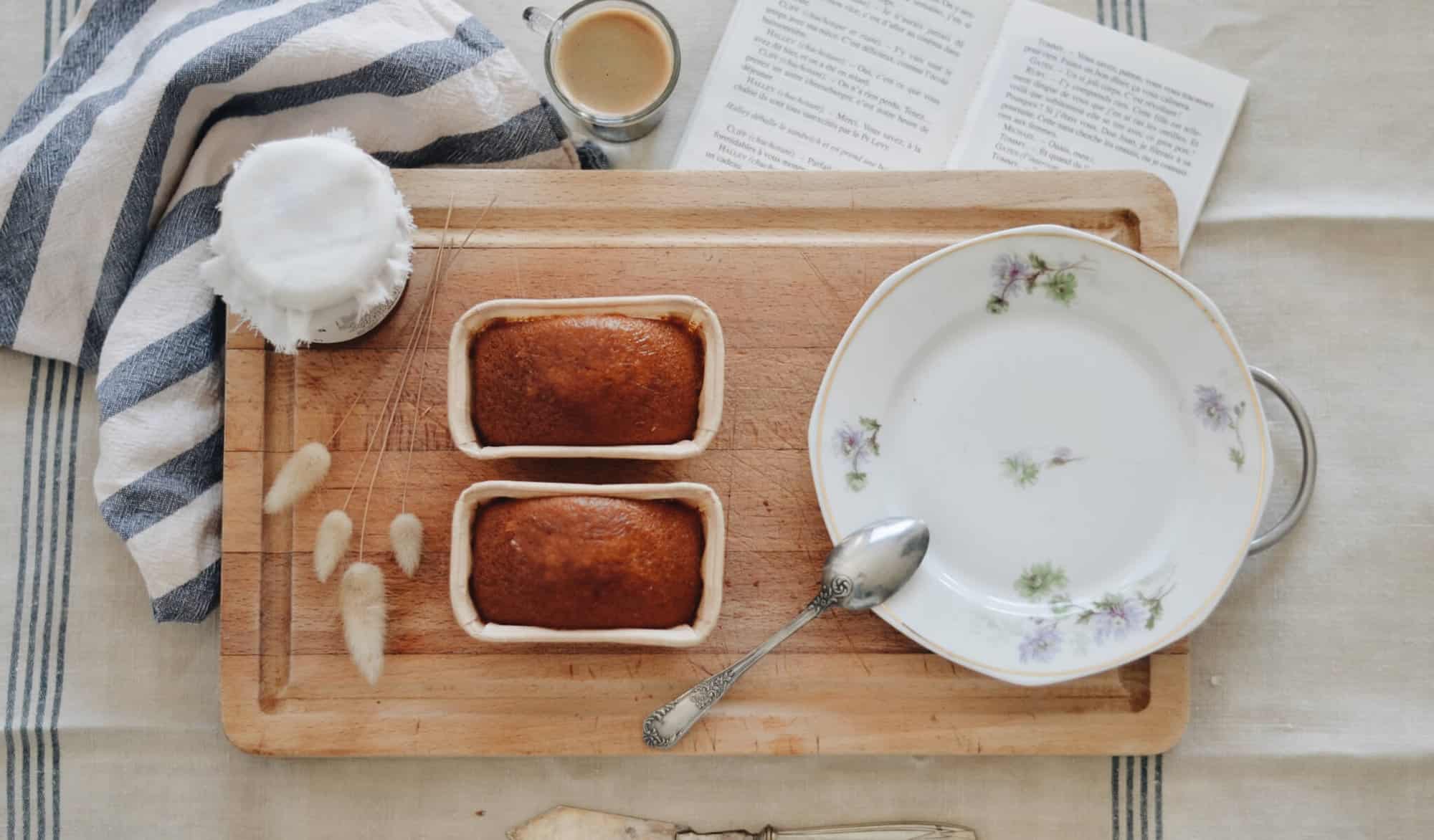 Left: a breakfast set with a white plate, wooden board, 2 brown cupcakes, and a cup of coffee.