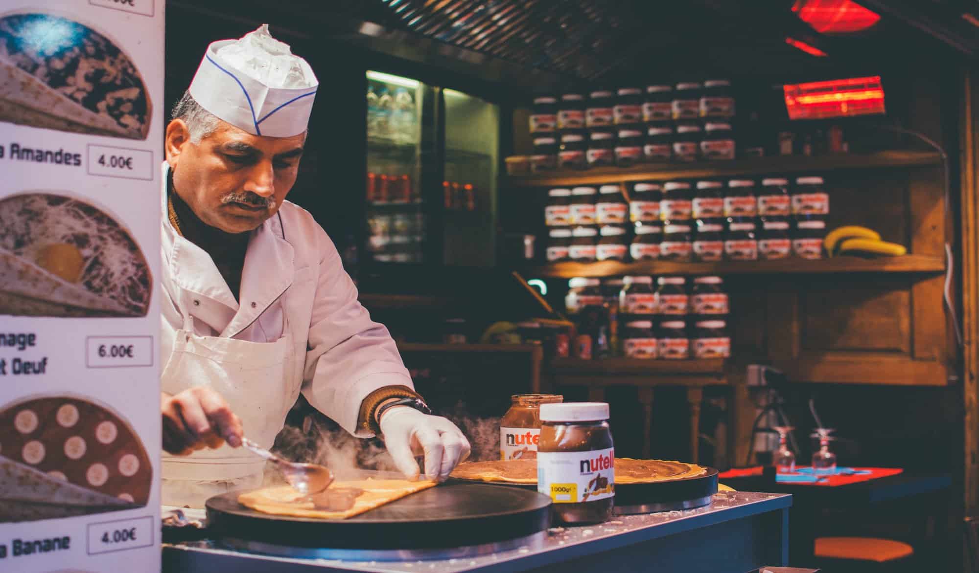 A man in a white uniform makes crepes with a serving of Nutella hazelnut spread.