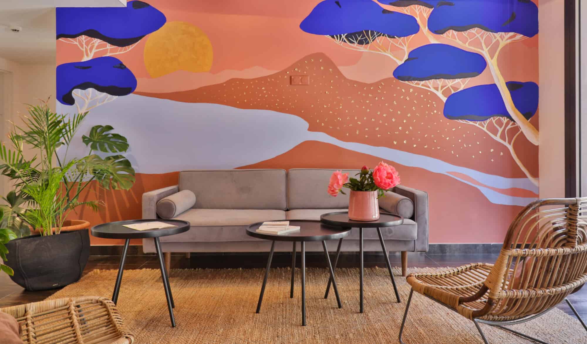 A hotel lobby with pink and blue painted walls, wooden chairs, and black coffee tables.