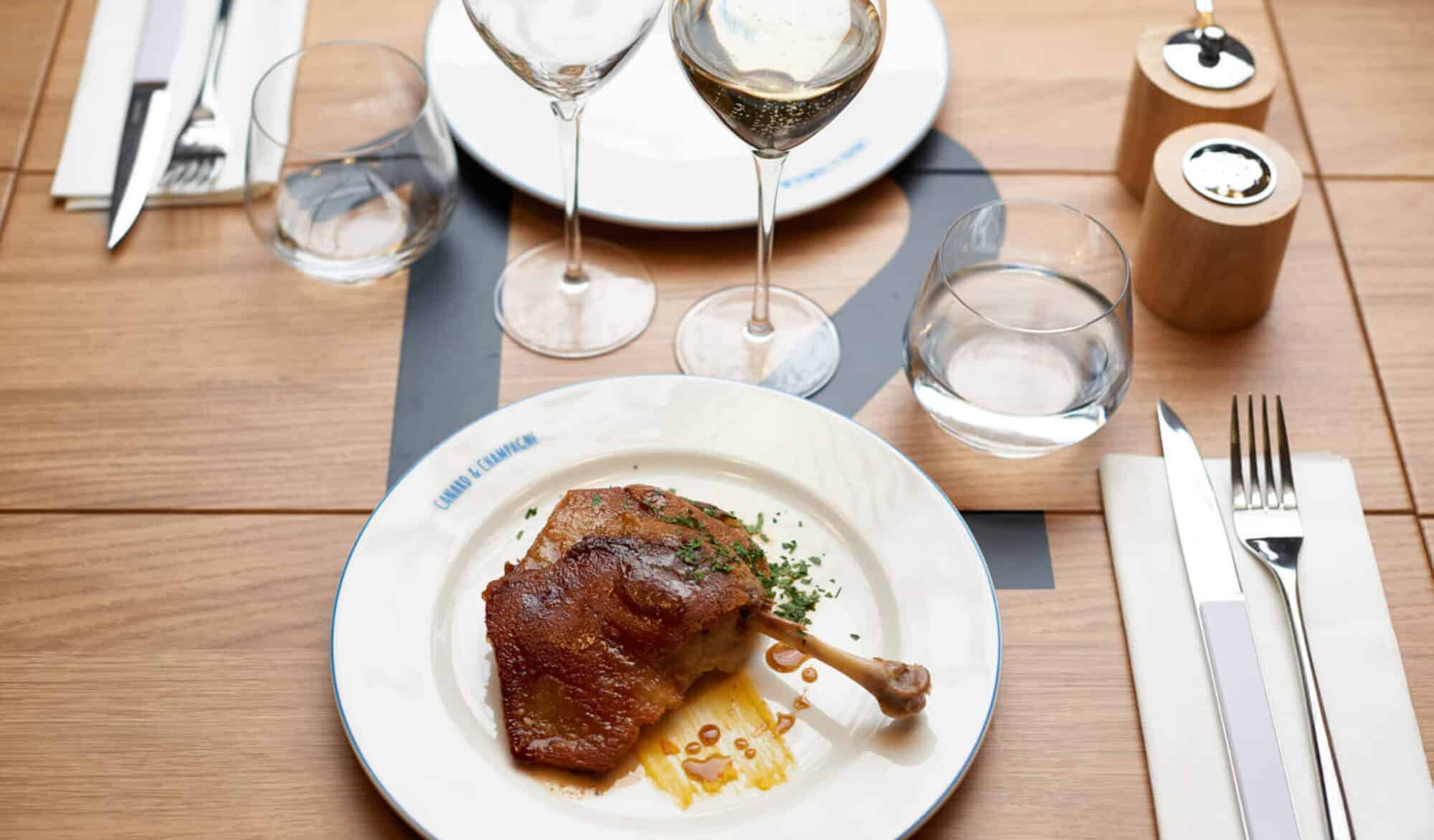 A restaurant table with a dish called duck confit and glasses of champagne