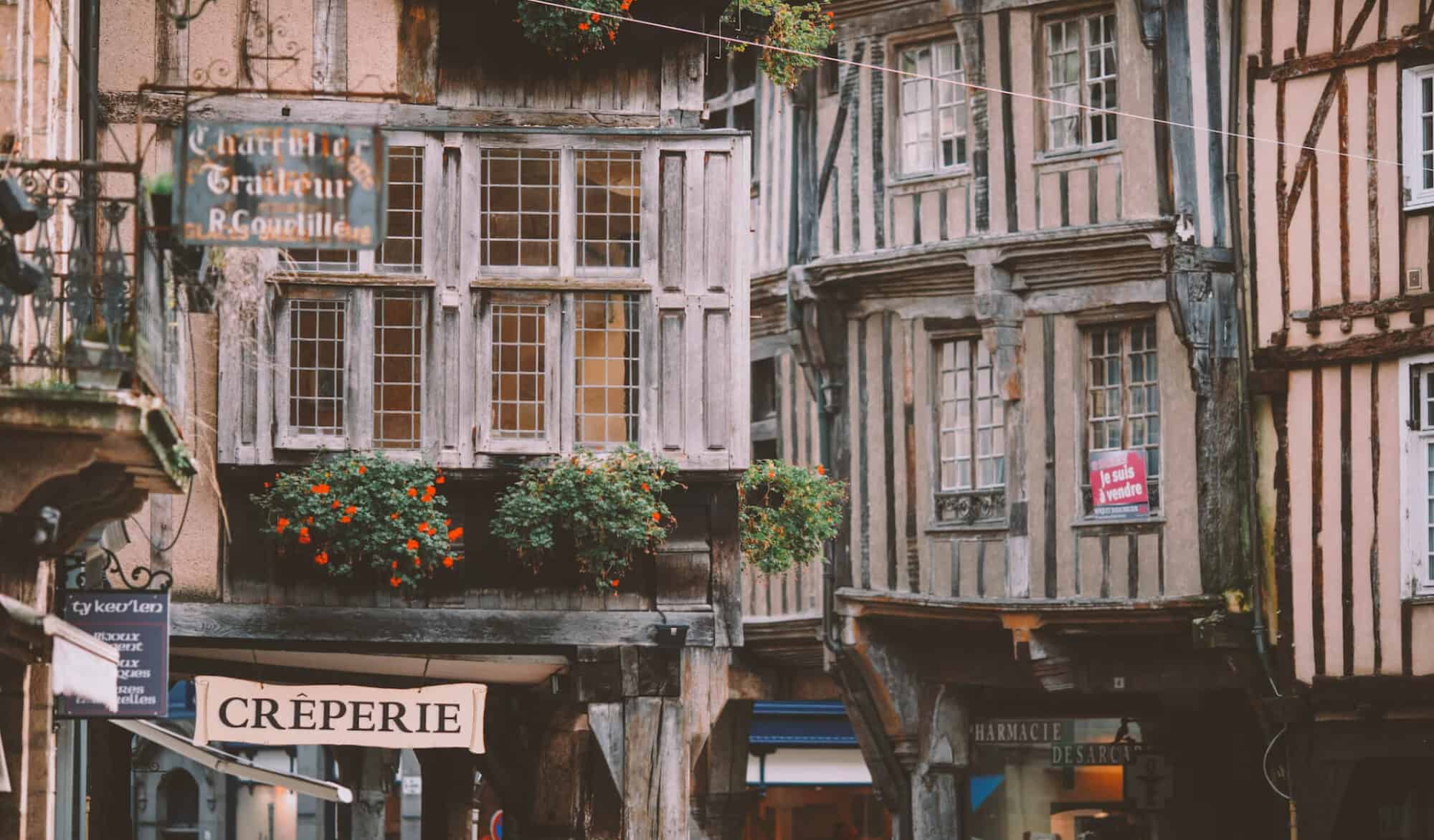 A medieval city full of wooden houses, with shrubs of flowers, and a creperie sign.