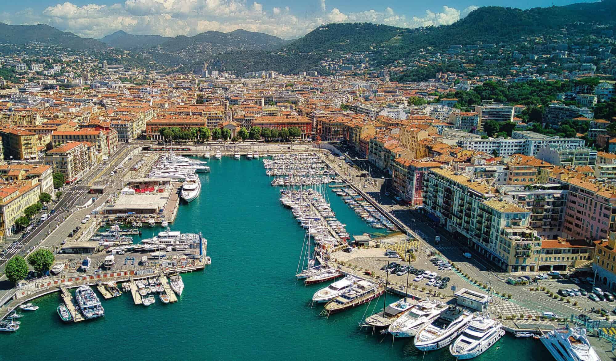 An aerial view of Nice's harbor with boats in dock. The water is a brilliant blue and the sun is shining.