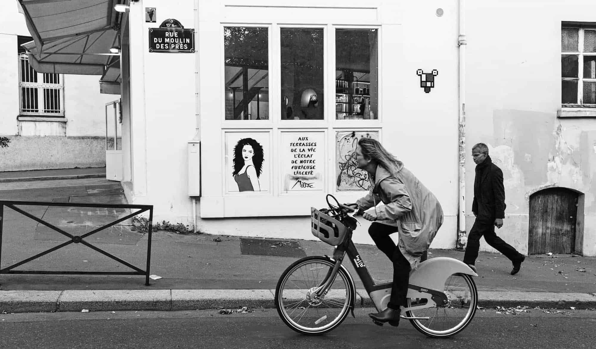 A woman in a trench coat rides a bike in Paris.