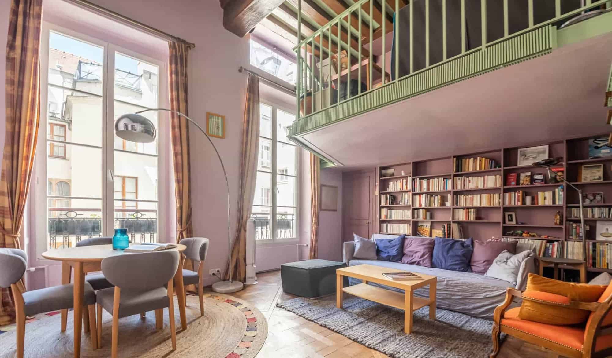 A Parisian loft apartment with purple walls, brown curtains, and gray chairs. 