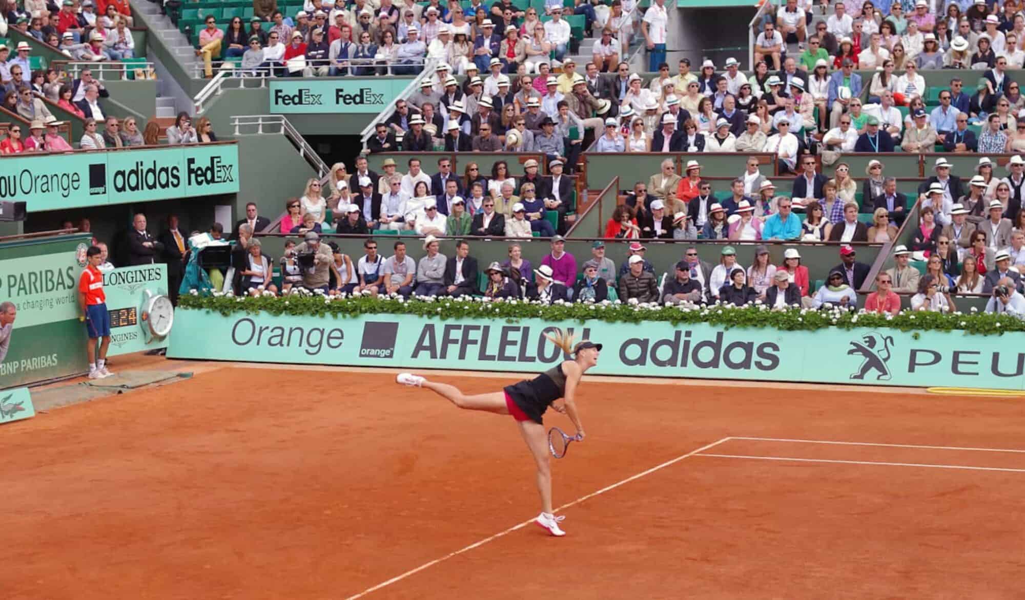 Nesta partida em Roland Garros ou no Aberto da França, uma tenista serve com seu traje preto enquanto uma multidão de espectadores assiste.