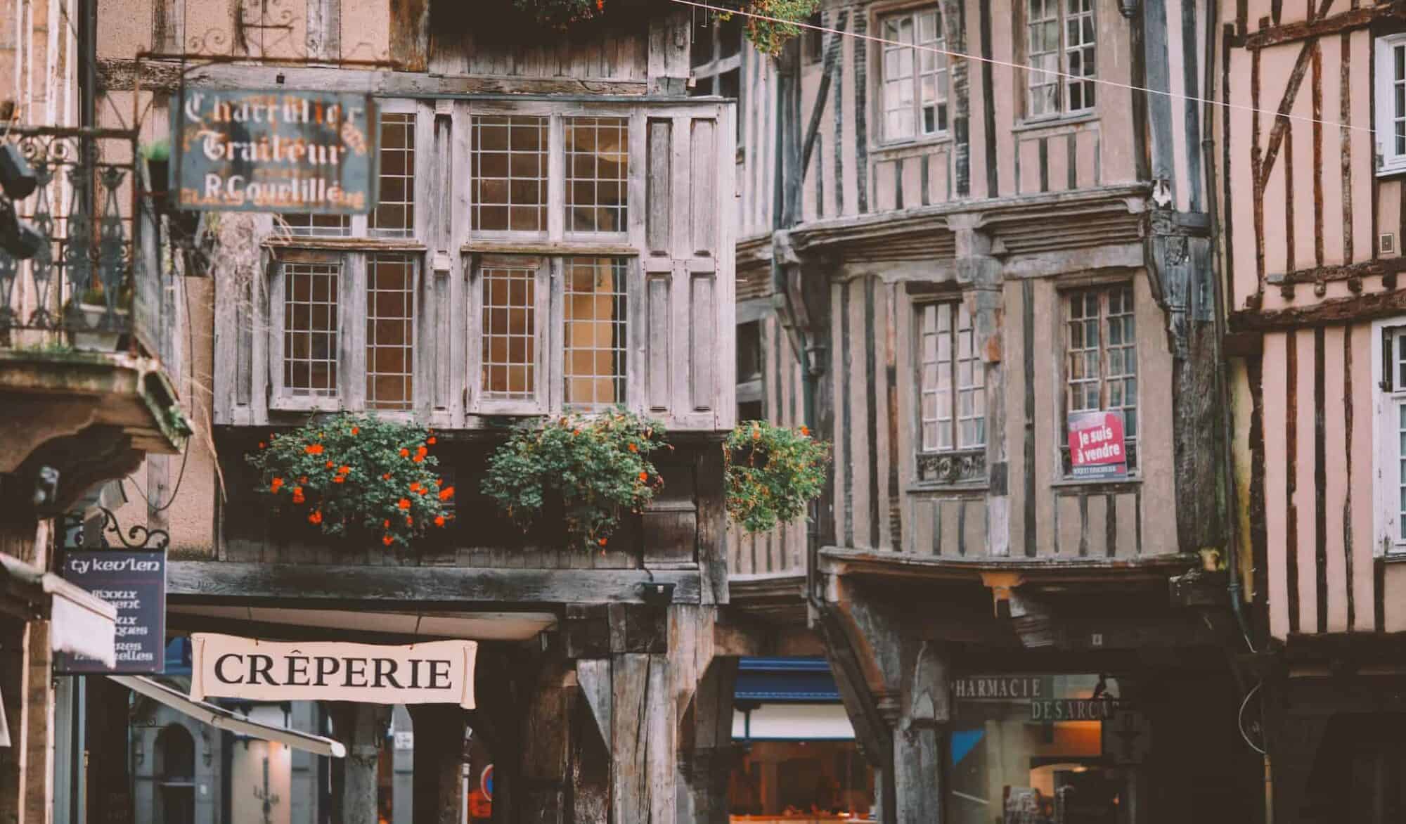 A charming old French town, full of wooden buildings with flowers, with a crepe shop on the left side.