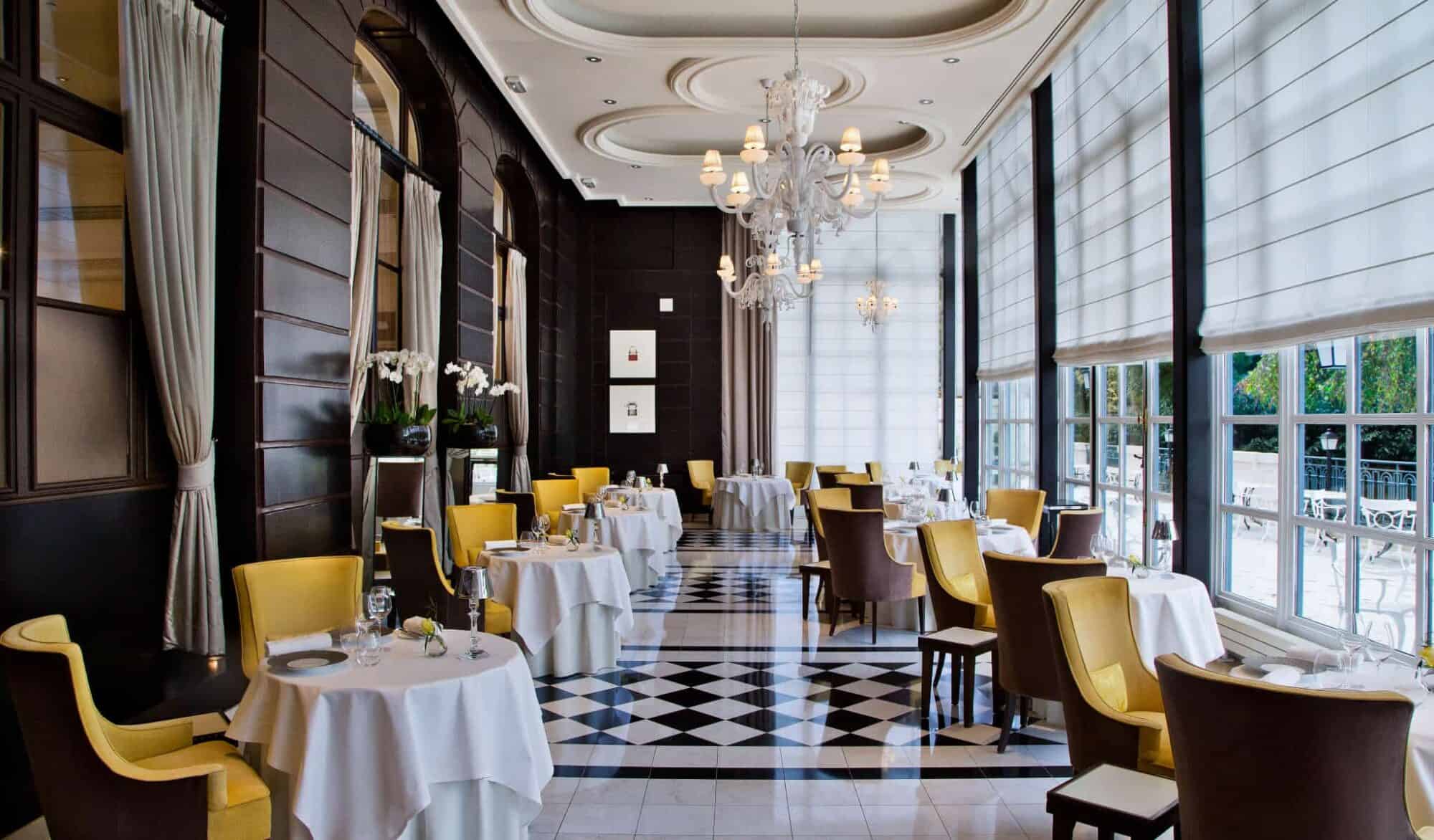Left: The interiors of Gordon Ramsay Au Trianon with yellow chairs, white rounded tables and brown wooden walls.