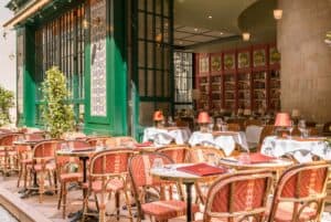 The bright terrace of Brasserie des Pres, with orange hued wicker chairs and green paint on the exterior of the building.