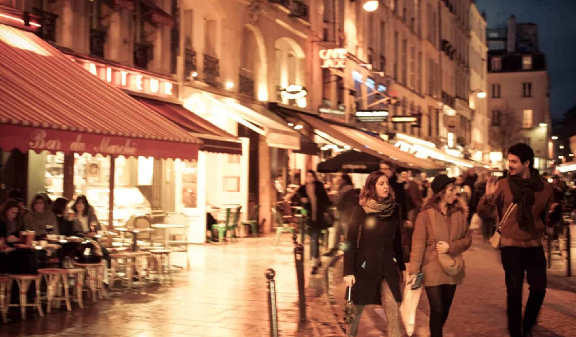 Three young Parisians strolling at night on a lit up Parisian boulevard.