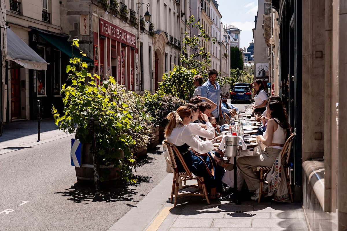 Um terraço na calçada em Paris com pessoas aproveitando o clima quente em um dia ensolarado de Paris.