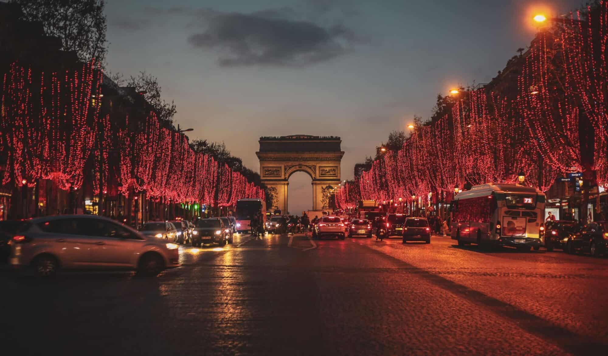 The Arc de Triomphe at night during Christmas with a row of trees with festive red lights.