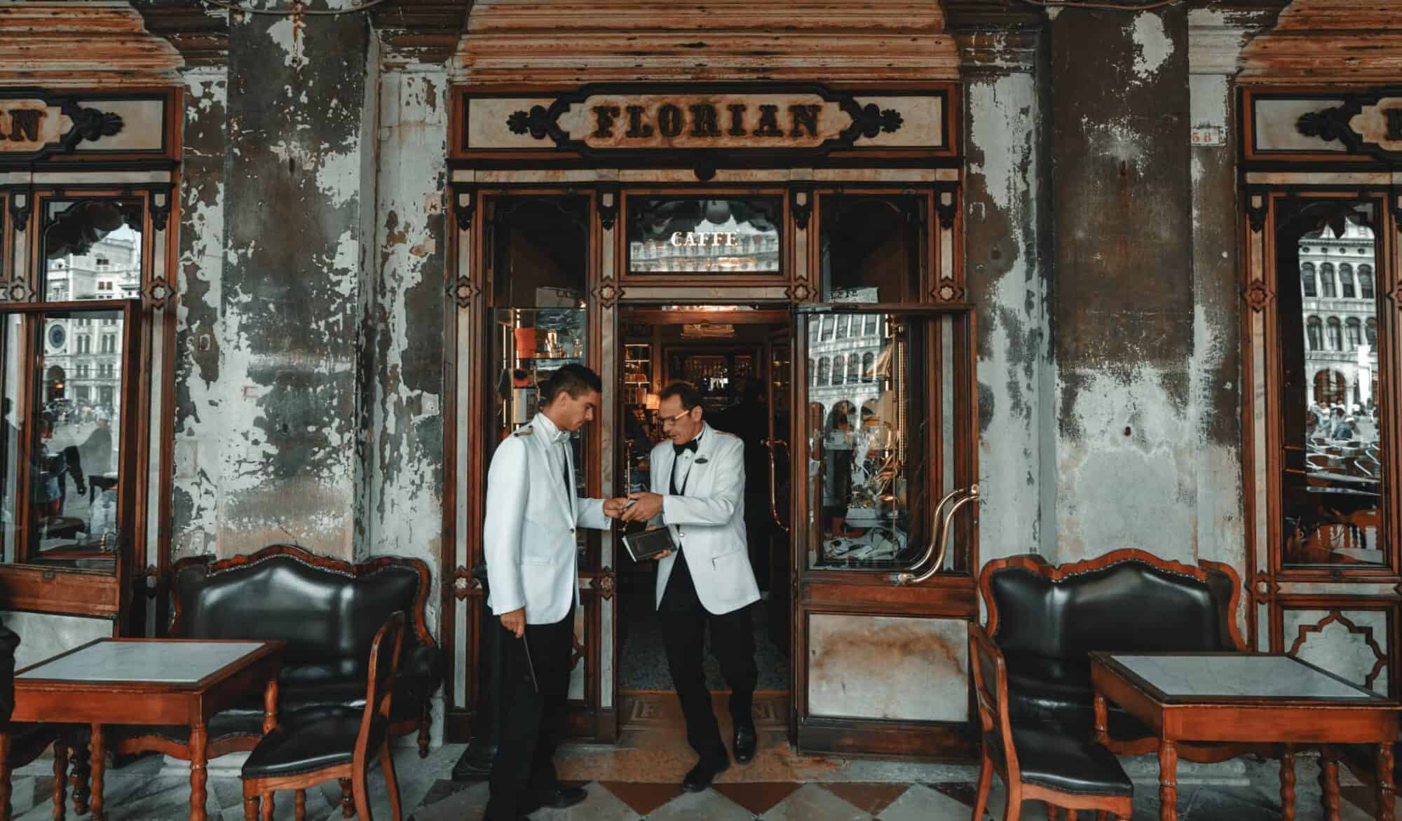 Two waiters in white jackets stand outside the Florian caffè in Italy.