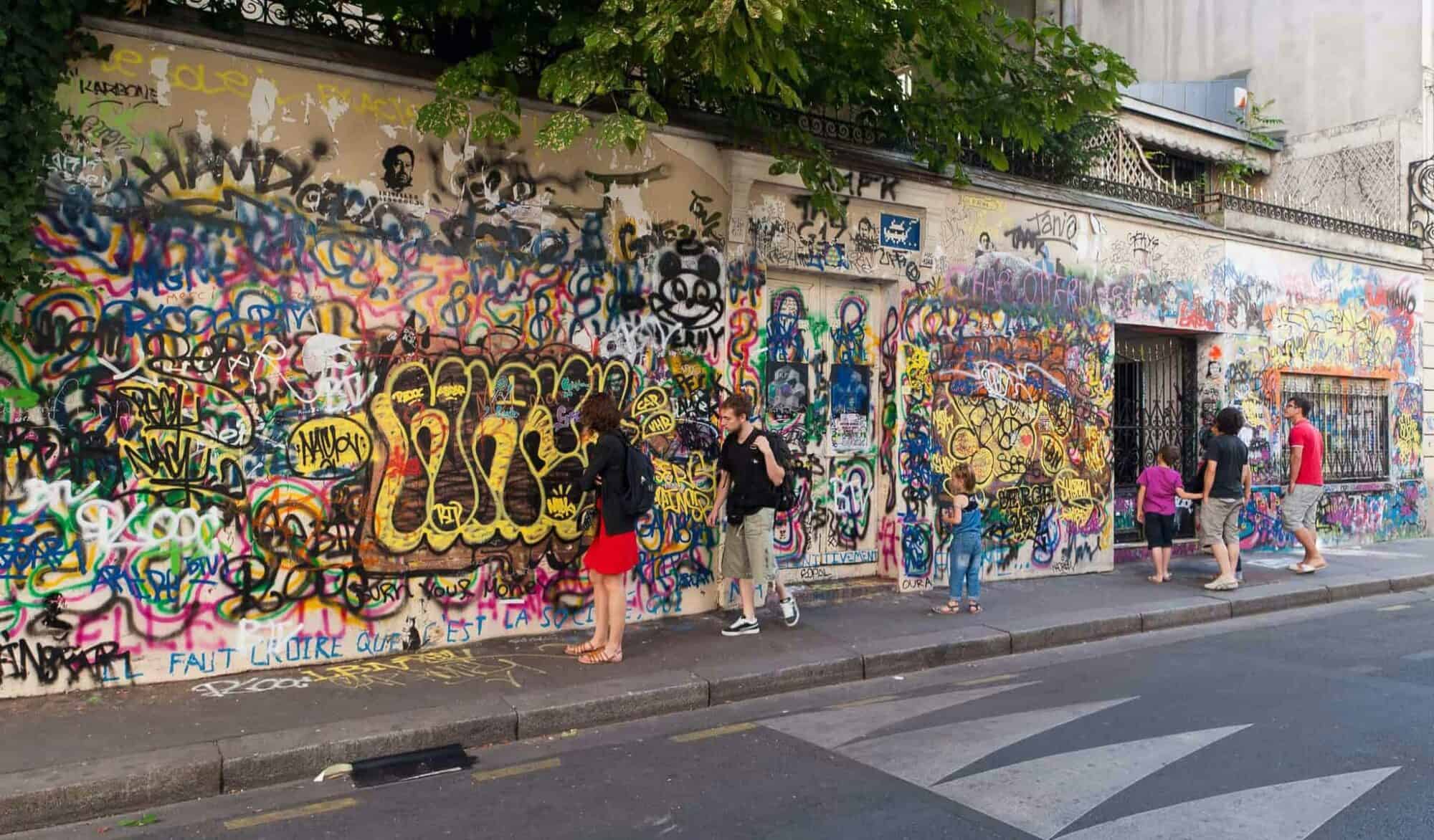 The exterior of Serge Gainsbourg's house in Paris, covered in colorful graffiti with two people walking past.