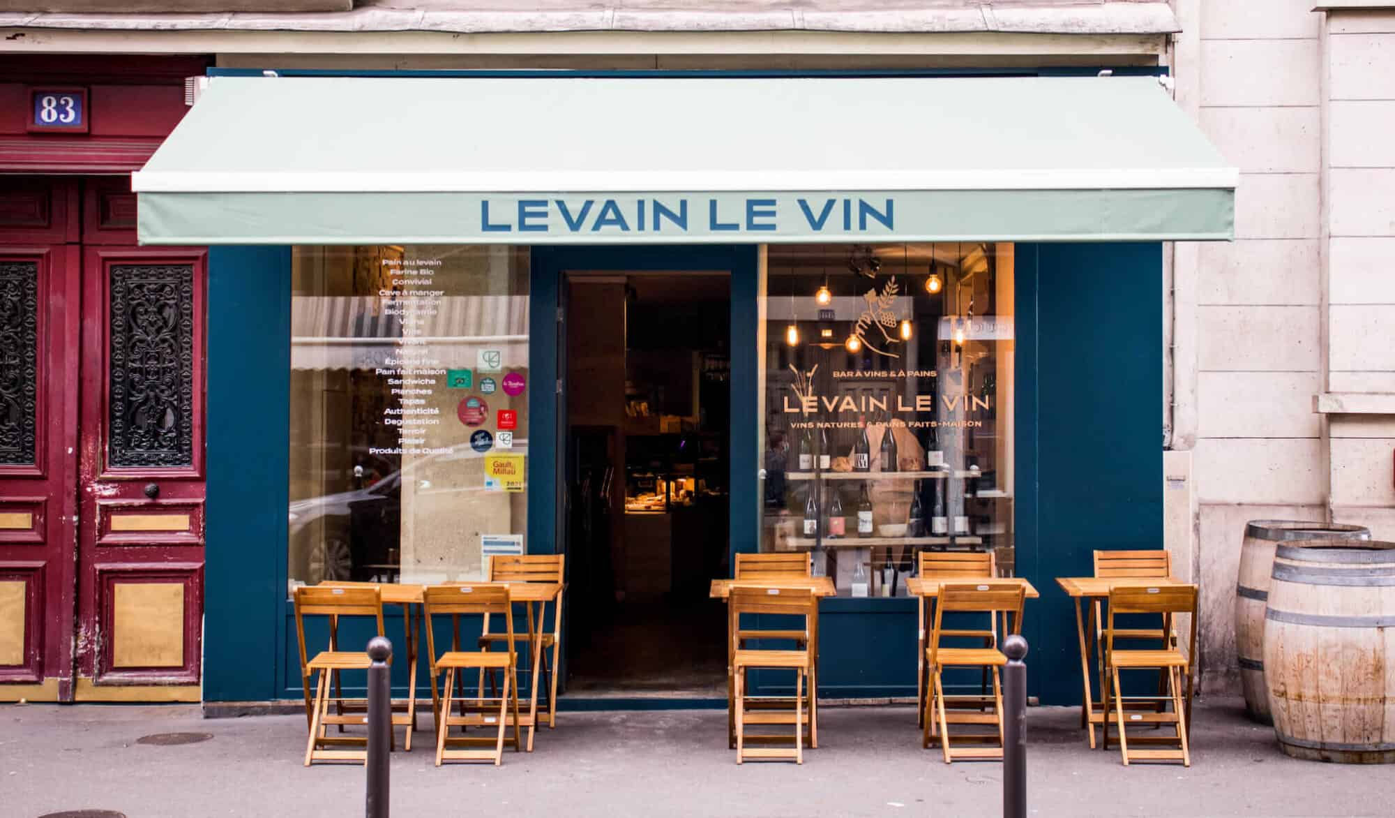 A wine bar in Paris called Levain Le Vin with its blue walled storefront, wooden chairs, and light blue awning.