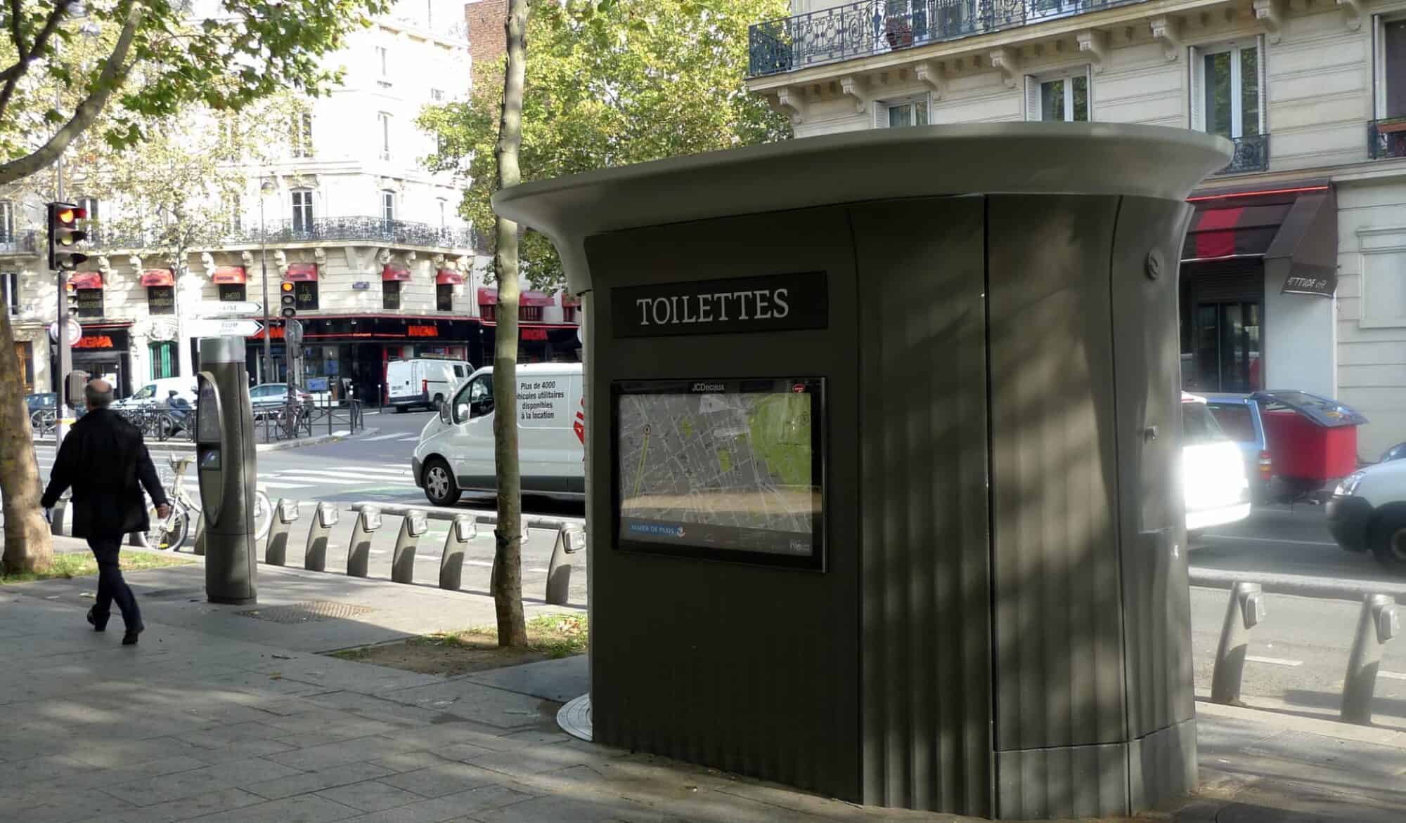 A public toilet photographed from the outside on a Paris street on a sunny day.