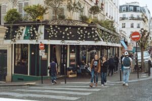 A mother and teen daughter walk past a Paris cafe while people pass by walking in the other direction carrying backpacks.