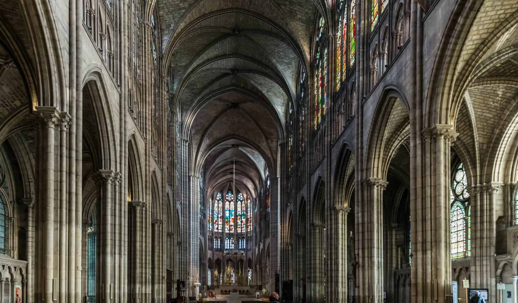 The interior of the Gothic Basilique Saint Denis in Paris with soaring ceilings, stained glass windows and stone interiors.