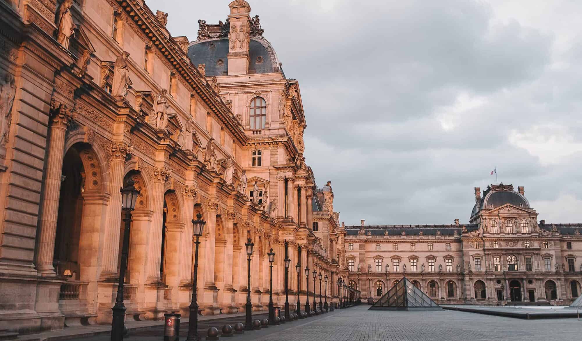 The courtyard of the Louvre Museum at the golden hour, with the iconic glass Pyramid straight ahead.
