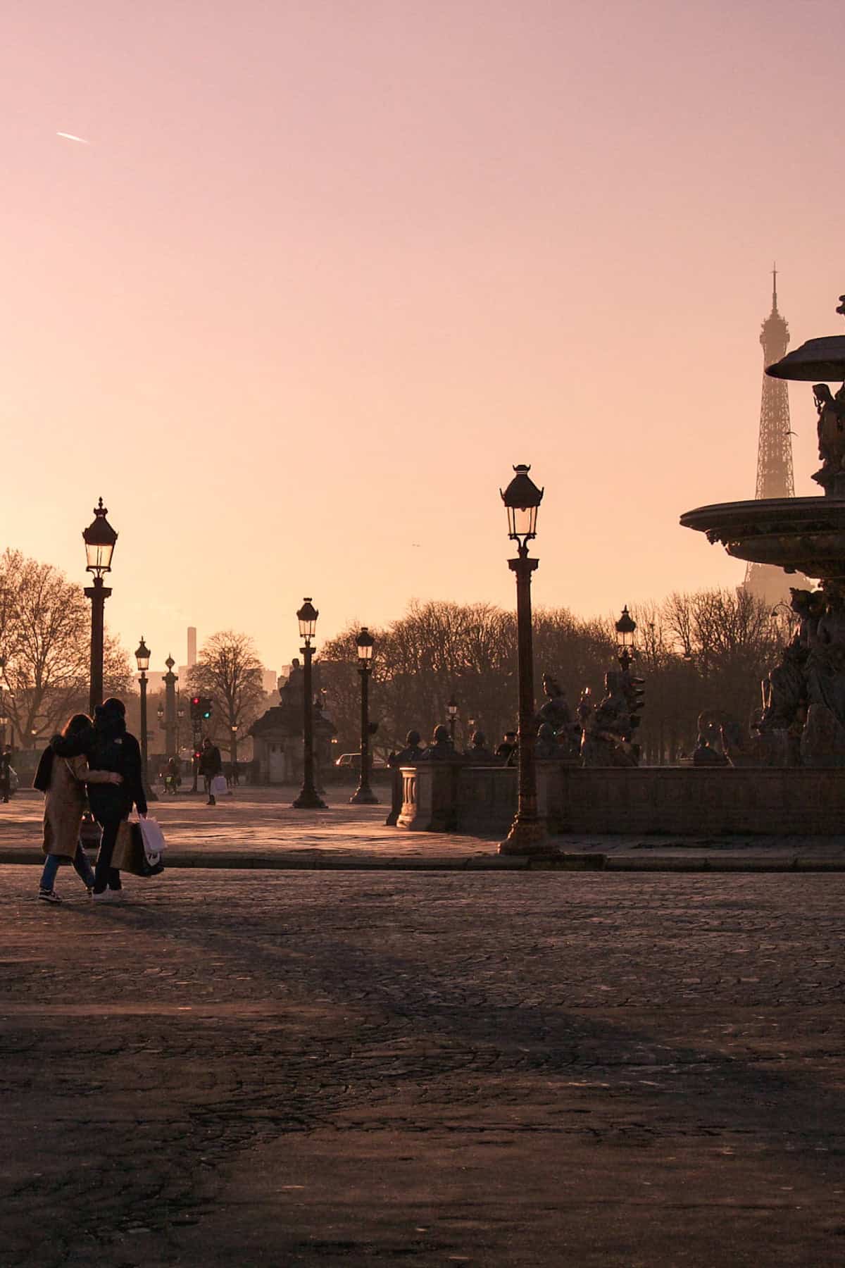 Two lovers walking with their arms around each other at sunset in Paris' Place de la Concorde, with a view of the Eiffel Tower 