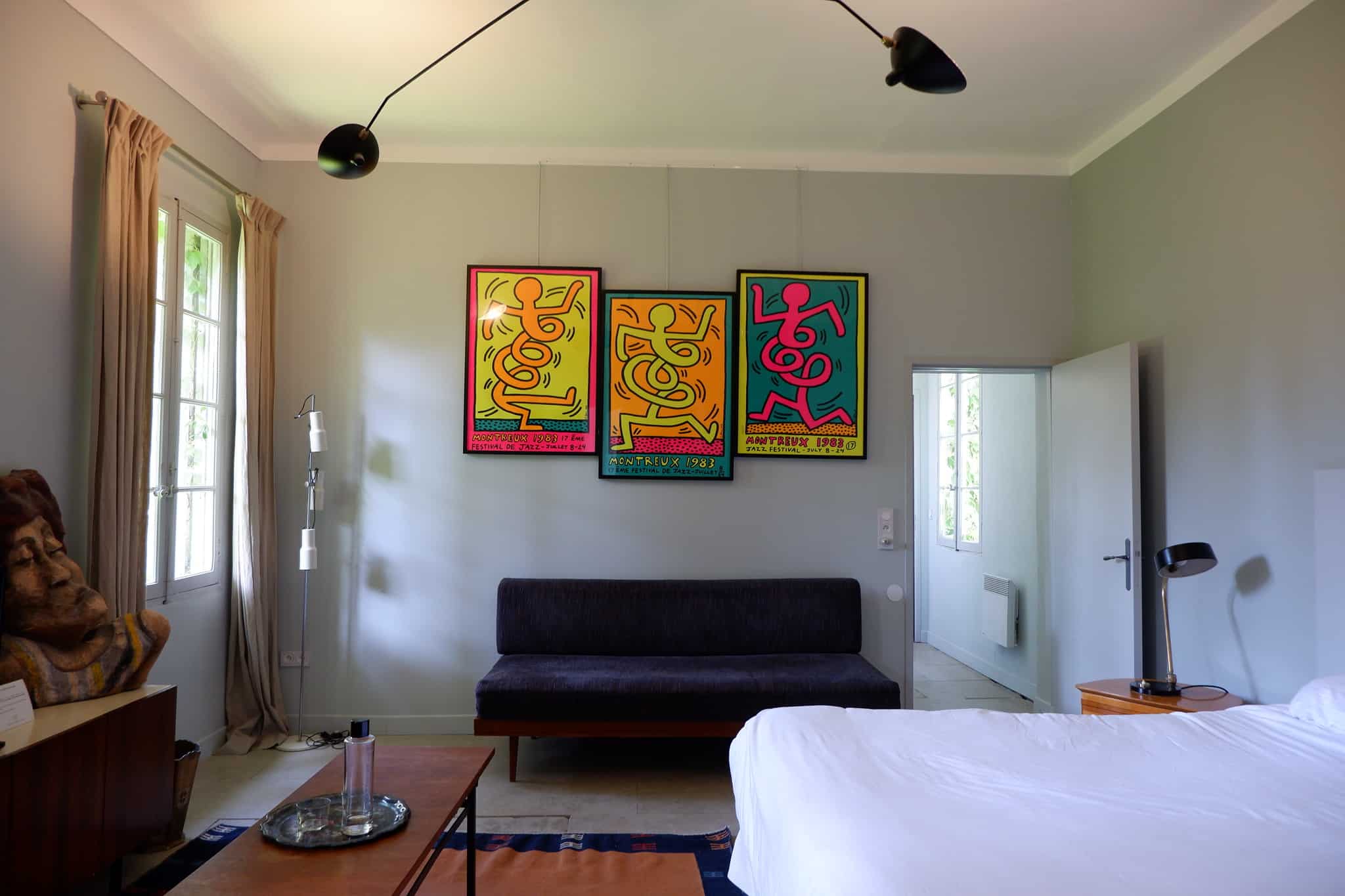 a room at La Mas de Lafeuillade with a white bed, brightly colored artwork and dark futon underneath.