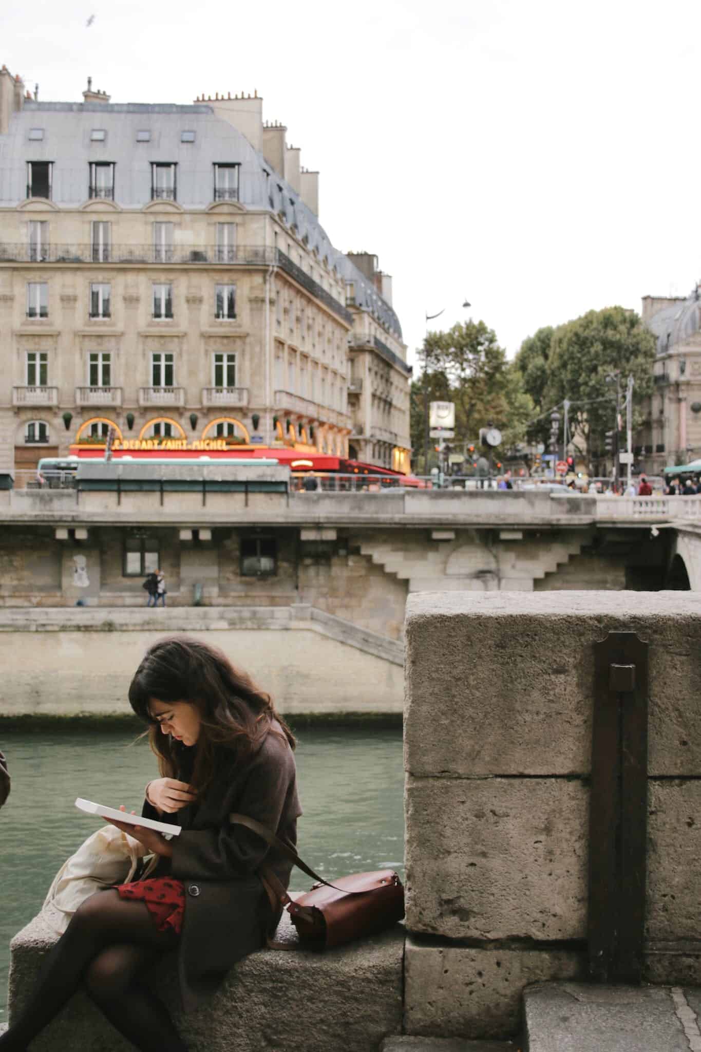 A woman reading a book beside the Seine River in Paris. 