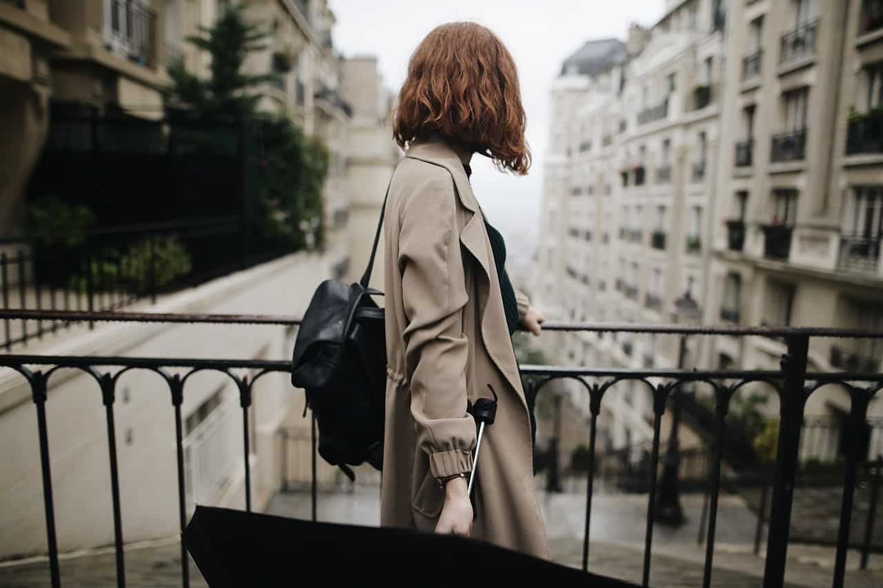 a woman in a trench coat walks with an umbrella and black backpack on a cloudy Paris day.