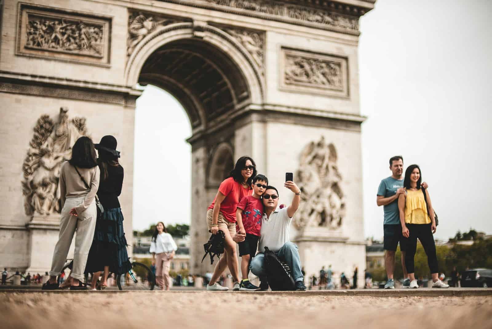 photography of family during daytime in front of the Arc de Triomphe taking a selfie photo.