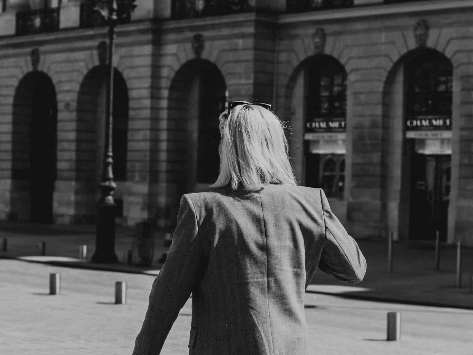 a woman walking down a street past a tall Parisian building