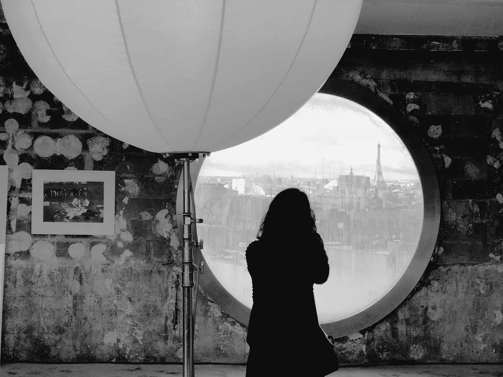 a woman standing in front of a round window with a view of the Eiffel Tower