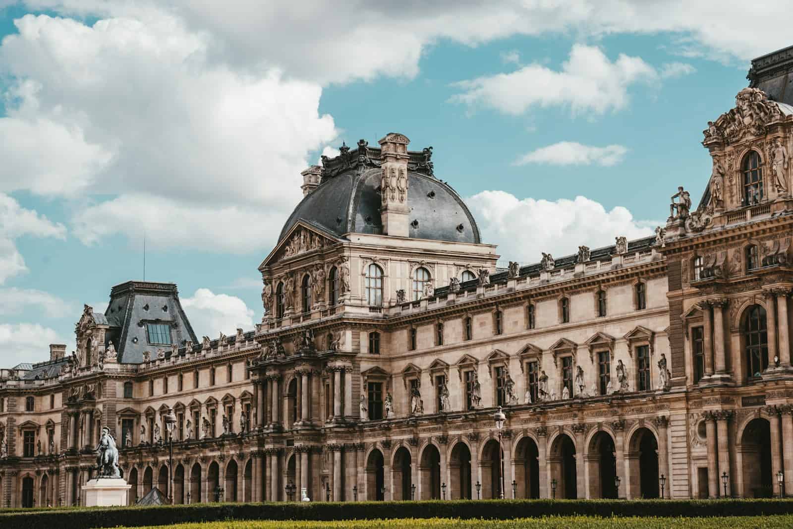 O exterior do Louvre em um dia parcialmente nublado. 