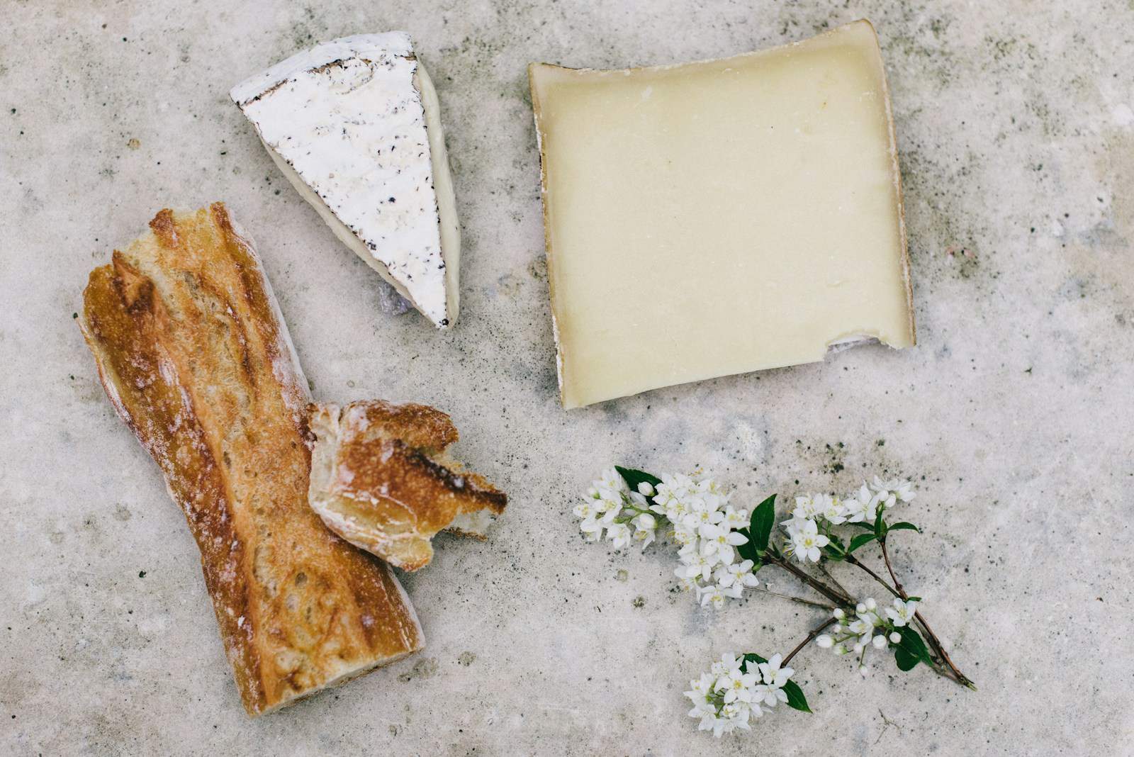 Cheese and a baguette portion beside white petaled flower.