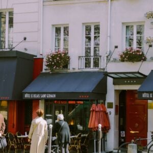 a couple of people stand outside a Paris cafe on a sunny day.