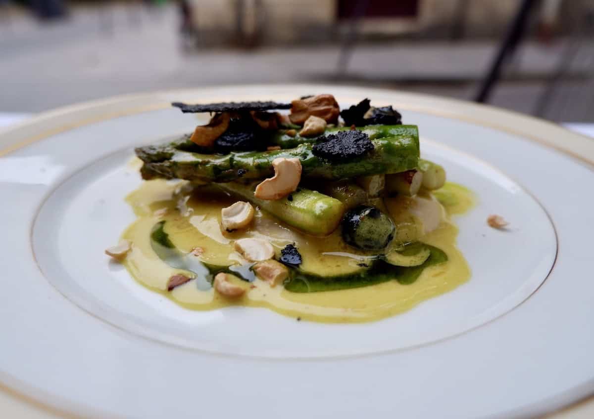 A starter of asparagus with a yellow sauce, garnished with some nuts served on a white plate.