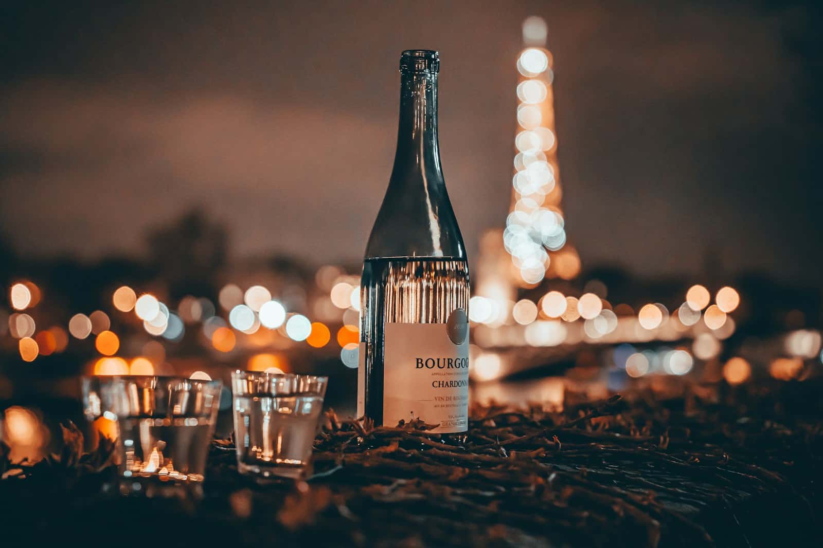 uma garrafa de vinho em cima de uma mesa com a Torre Eiffel iluminada ao fundo.