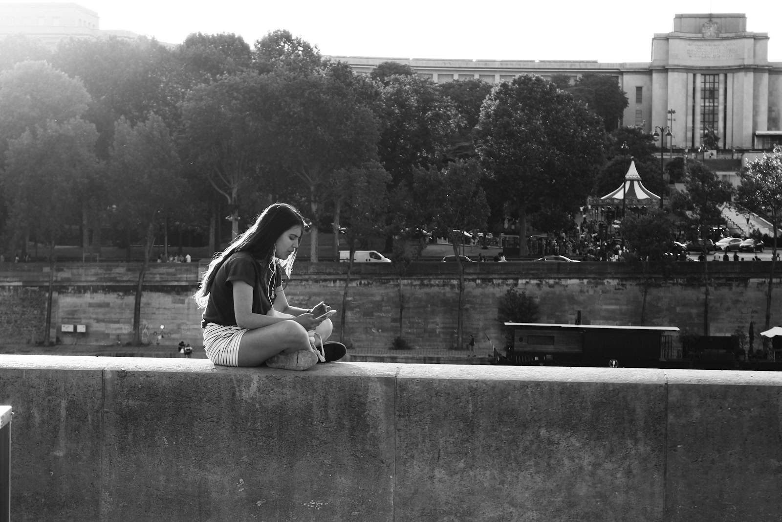 A young woman in white shorts and a black shirt sitting on concrete wall along the Seine.