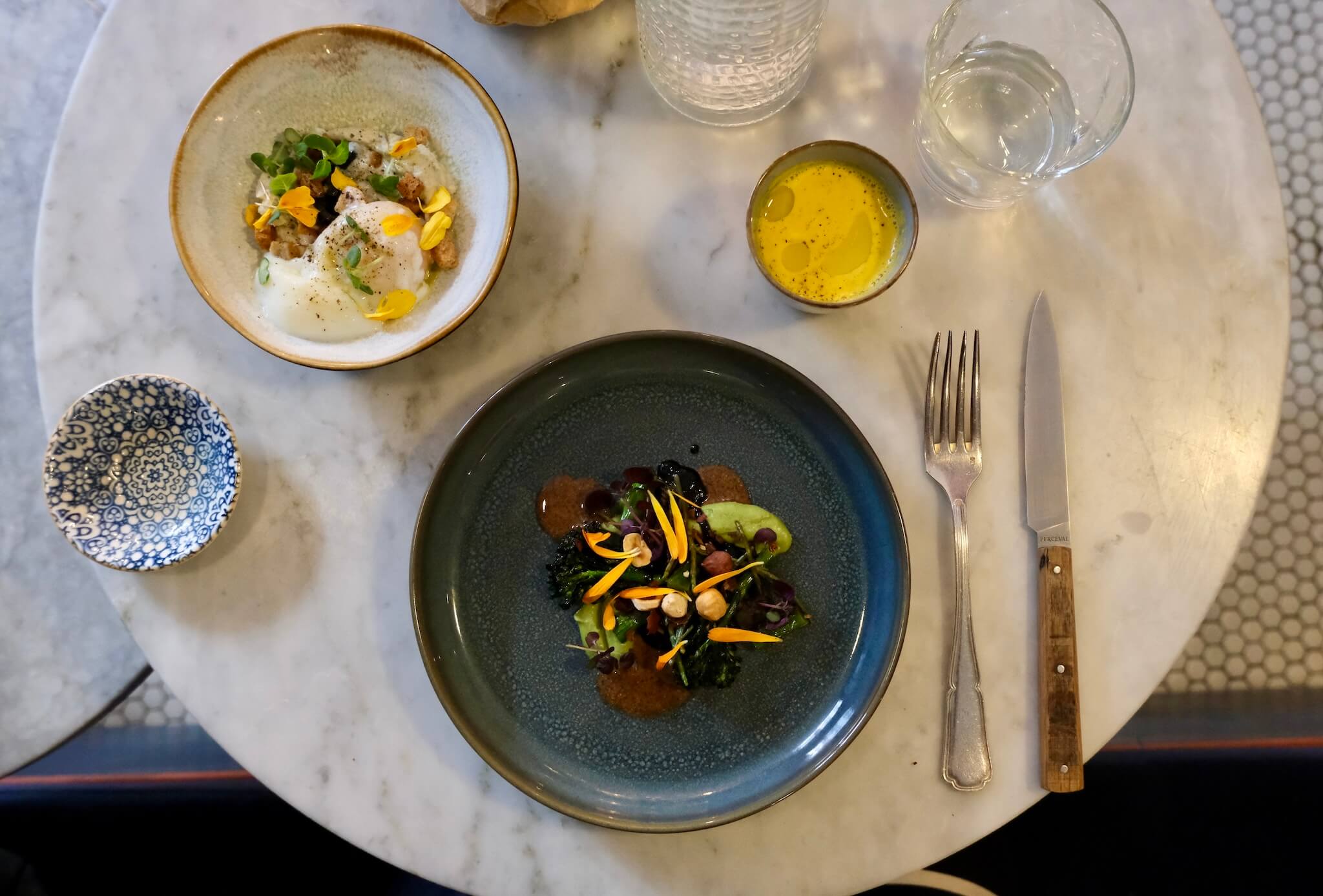 A roasted broccolini starter dish on a blue plate at Pouliche. Off to the side is the oeuf parfait starter.