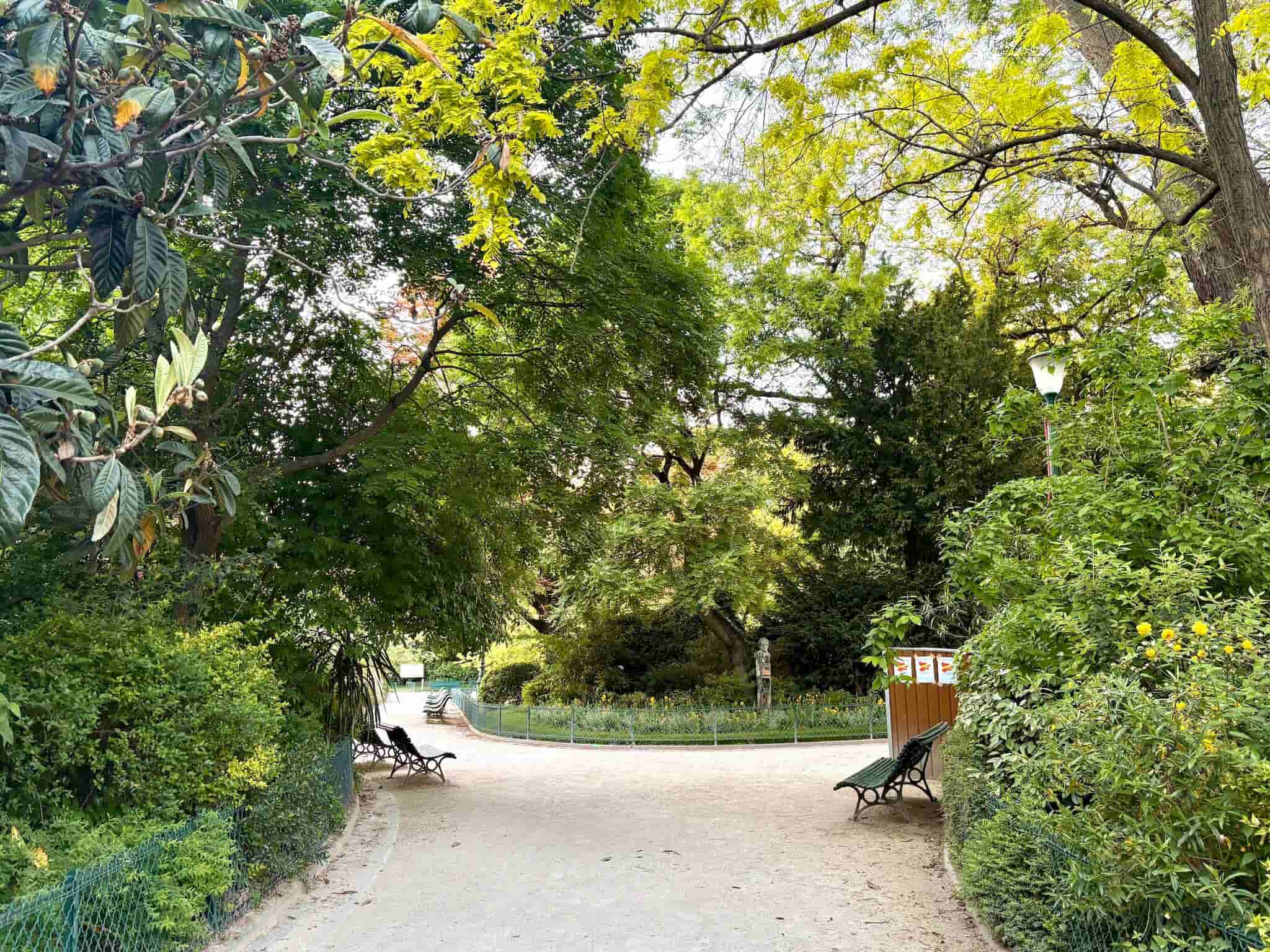Park benches on a path at Square du Temple, surrounded by bushes trees.