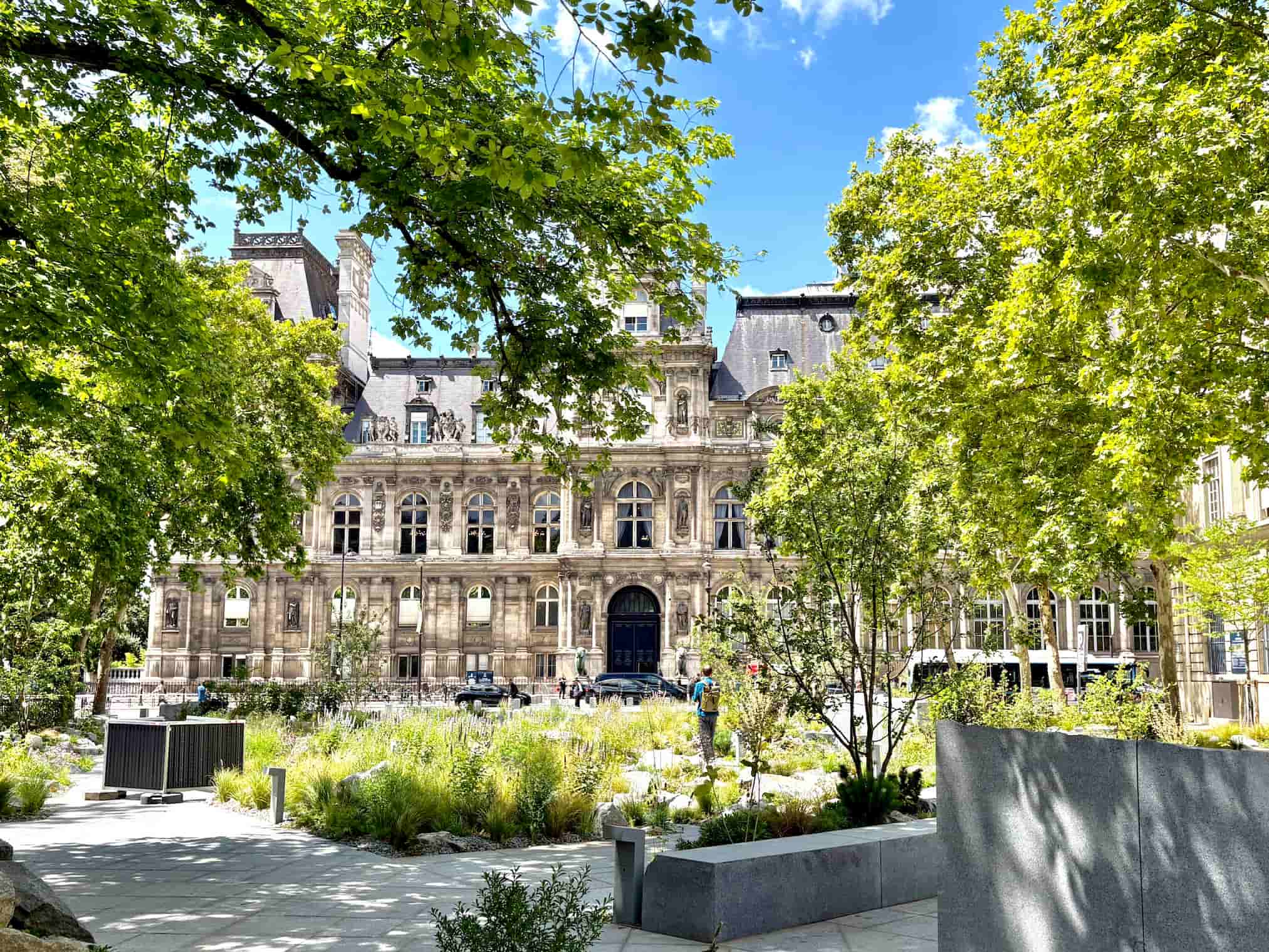 Hôtel de Ville view from memorial garden. Green trees and blue sky.