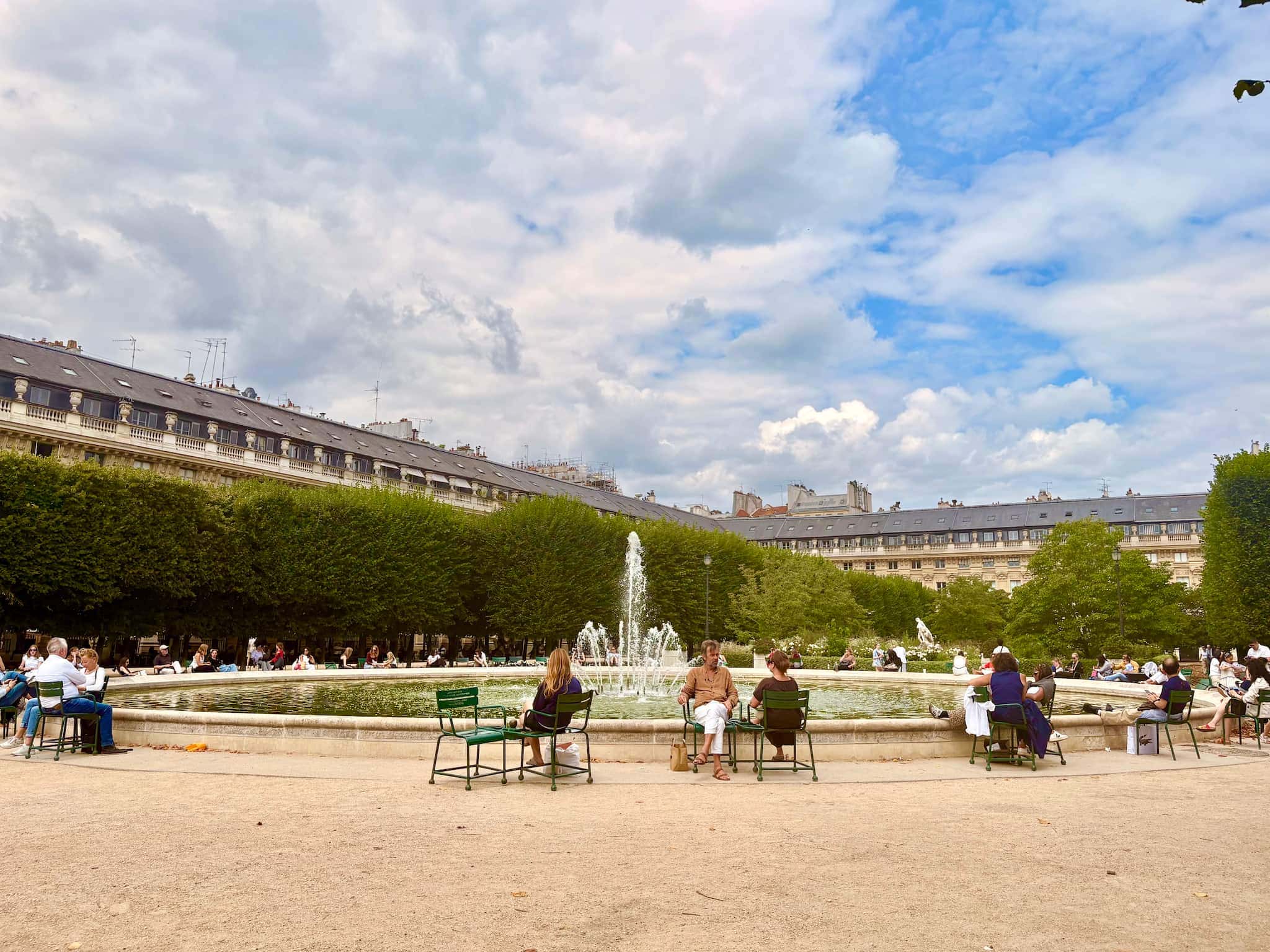 Fountain at Palais Royal gardens in Paris, people sit around the fountain in green chairs.