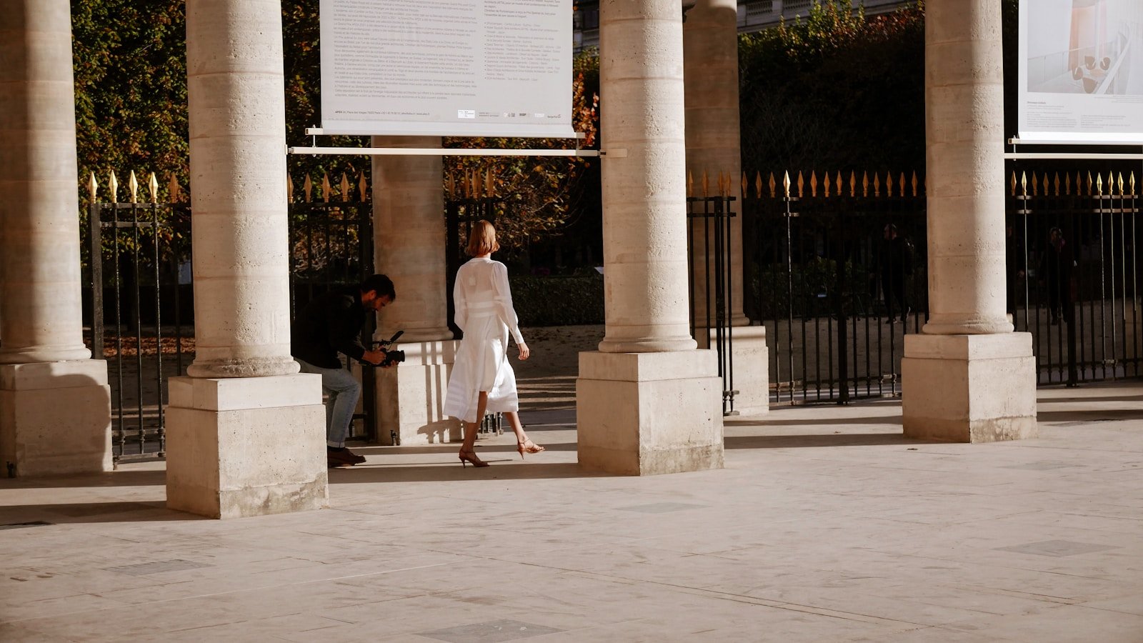 a woman walking down a sidewalk next to tall pillars.