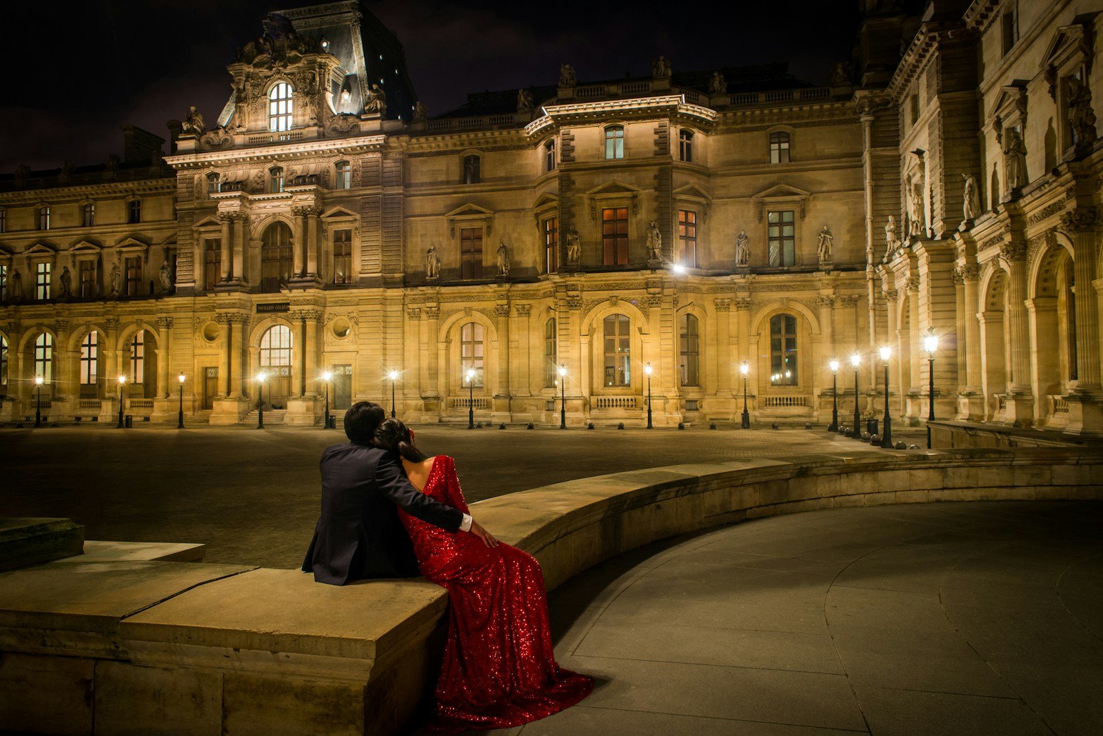 a man and a woman sitting on a ledge in front of a building in Paris at night.