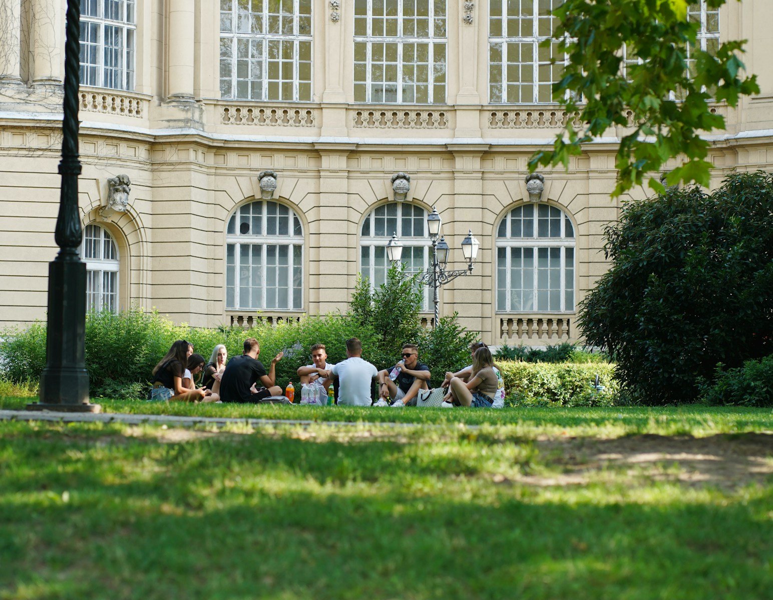 people sitting on green grass field near white concrete building during daytime.