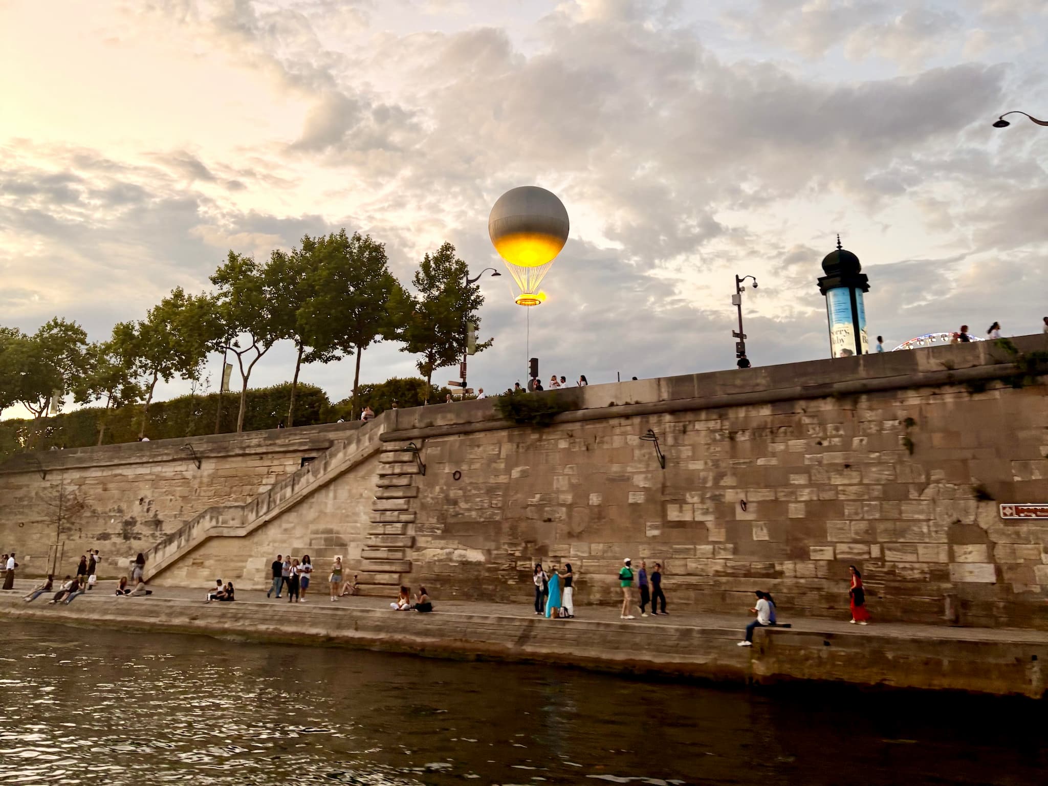 People sit by the Seine as the Olympic cauldron floats into the evening sky.