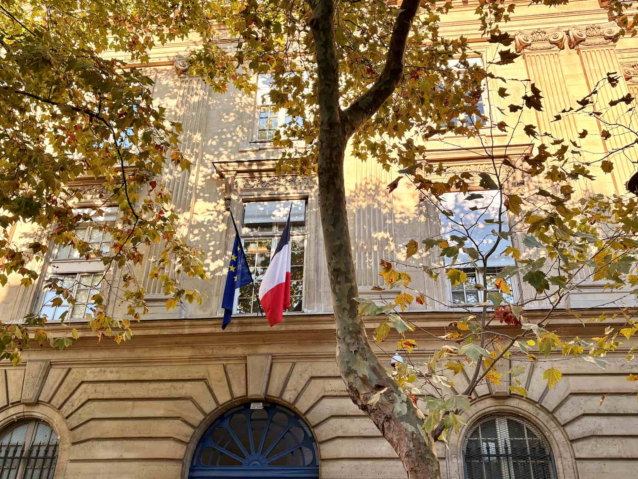 French and EU flags on a Paris building. Trees with yellow leaves in foreground.