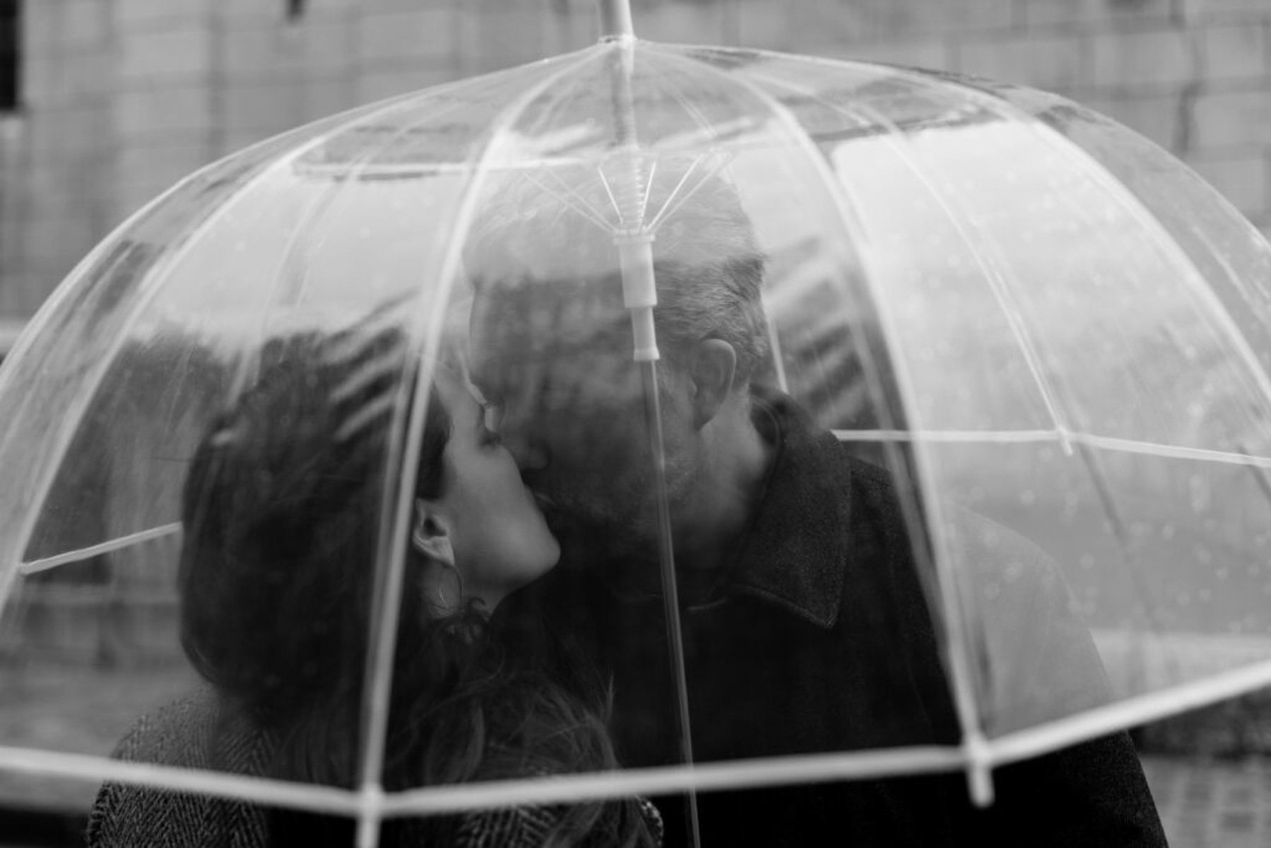 A couple kissing under a clear umbrella in the rain in Paris.