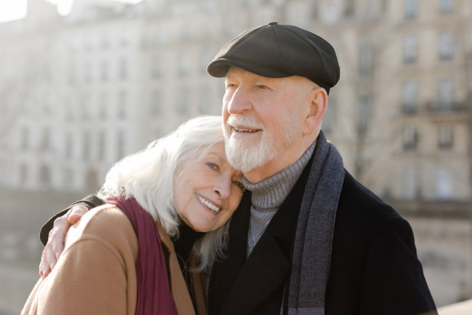 An older couple hugging on a bridge in Paris on a winter day.